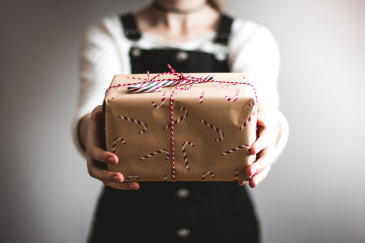 A person holding out a small gift wrapped in brown paper and tied with string