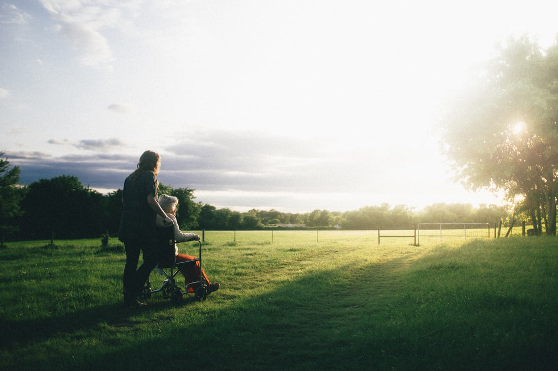 An adult child walking outdoors at sunset beside an older parent