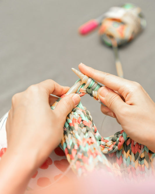 An older woman sitting comfortably and crocheting with soft yarn